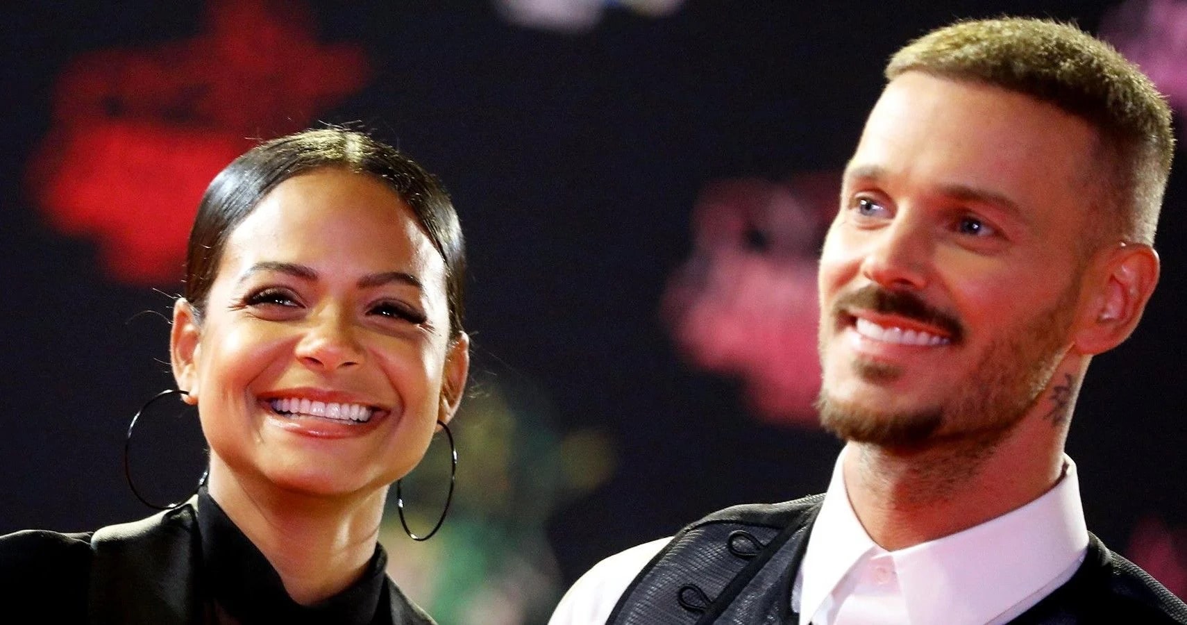 M. Pokora in a white shirt with his wife in a black dress.
